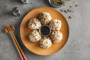 Wooden plate with tasty baozi dumplings and sesame seeds served on grey table, top view