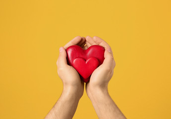 Man holding decorative hearts in hands on color background, closeup