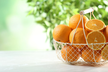 Basket with ripe oranges on table against blurred background. Space for text