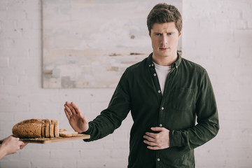 cropped view of woman holding cutting board with bread near handsome man with gluten allergy - obrazy, fototapety, plakaty