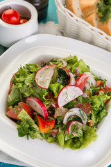 Fresh vegetable salad, radishes, tomatoes, lettuce, dill, blue wooden background
