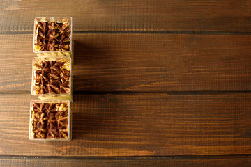 Three small cups of tiramisu dessert on brown wooden background. Place for text