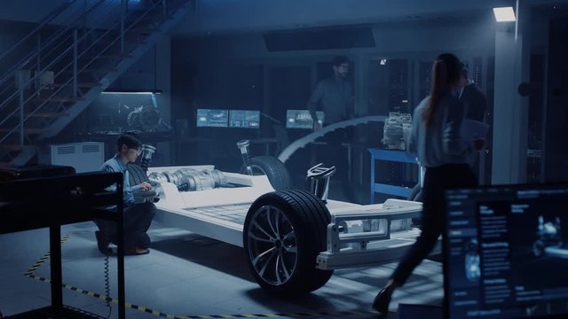 Automotive Design Engineers Work and Do Tests on Electric Car Chassis Prototype. In Innovation Laboratory Facility Concept Vehicle Frame Includes Wheels, Suspension, Engine and Battery.