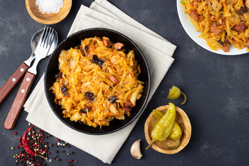 Traditional dish of polish cuisine - Bigos from fresh cabbage, meat and prunes. Top view. Dark background.
