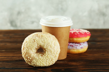 Vibrant composition of lush donut with colorful sprinkled icing and disposable paper cup on wood...