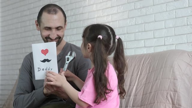 Father's day. A cute little girl gives her dad a postcard and a monkey wrench.