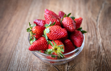 Fresh organic strawberries in a glass bowl on wooden table