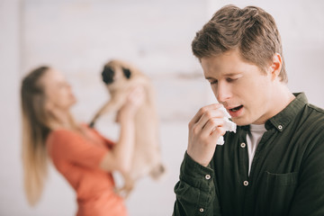selective focus of man having allergy and sneezing in tissue near woman with dog