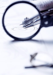 Fototapeta premium View of a compass through a magnifying glass on the background of a roll with drawings