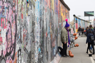 Close-up of graffiti at the East Side Gallery, section of the Berlin Wall in Berlin, Germany. Street musician and tourists in the background.