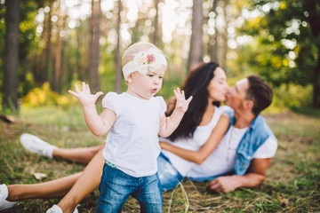 Fototapeta premium little girl one year on the background of parents resting lying on grass learning to walk on nature in the park. The first steps of a child in nature outside the city in the forest