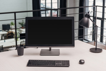 modern workplace with computer, coffee to go and lamp in office