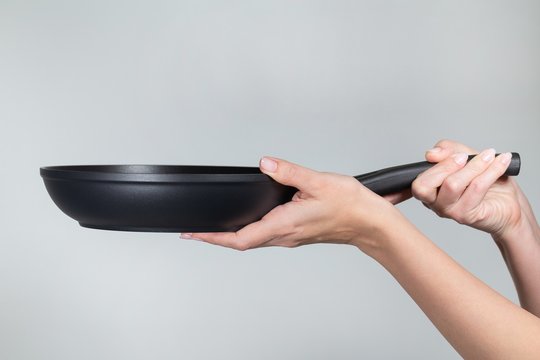 Closeup view of female hands holding new empty black frying pan with non-stick bottom. Horizontal color photography.