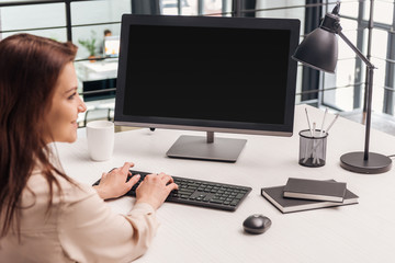 Fototapeta na wymiar selective focus of smiling woman using computer at workplace