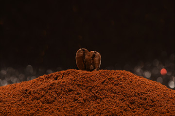 Two freshly roasted coffee beans stand on a handful of ground coffee on a bokeh background. Isolated macro. Post card, banner. Copy space.