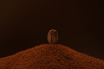 Fresh roasted coffee bean stands on a handful of ground coffee on a brown background. Isolated macro. Post card, banner. Copy space.