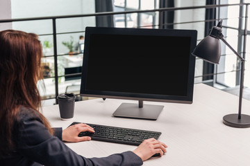 cropped view of woman using computer at workplace with lamp and coffee to go in modern office