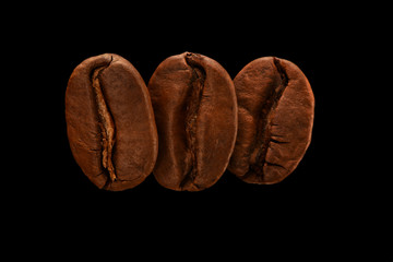 Three fresh roasted coffee beans isolated on a black background. Close up, macro. Post card, banner.