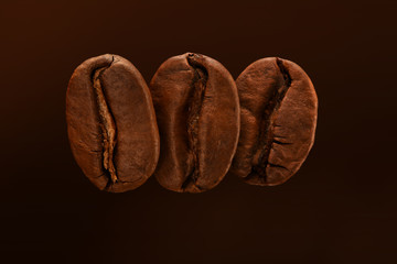 Three fresh roasted coffee beans isolated on a brown background. Close up, macro. Post card, banner.