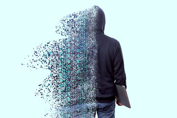 Back view of man in hood, hacker with laptop dispersing and disintegrating into particles of the...