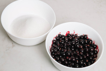 Black currant jam with sugar. Berries background. Top view, close-up. Black currant and sugar in different bowls in white