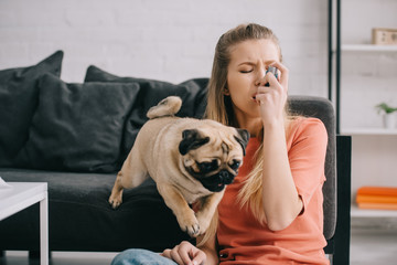 beautiful blonde woman allergic to dog using inhaler near pug at home
