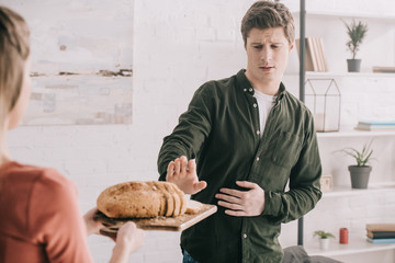 cropped view of woman holding cutting board with sliced bread near handsome man with gluten allergy