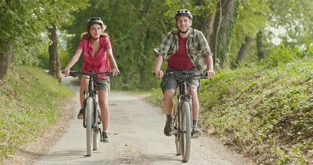 Romantic active couple riding e-bike bicycles mtb on a beutiful outdoor woods path.Wide shot.Friends italian trip in Umbria.4k slow motion - Powered by Adobe