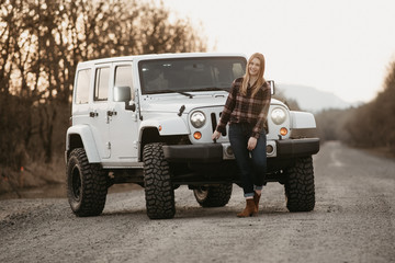 Young woman standing in empty dirt road with her SUV.