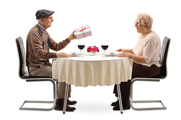 Elderly man giving a present to an elderly woman at a restaurant table