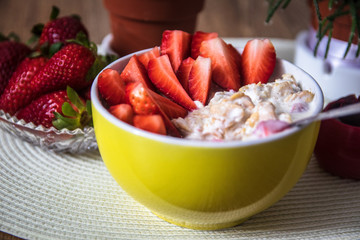 Fresh organic strawberries with muesli porridge in a yellow clay bowl