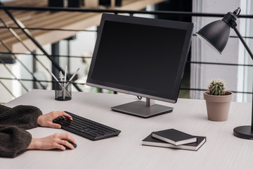 cropped view of woman using computer at workplace with stationery