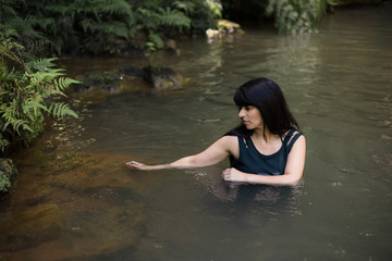 Fototapeta premium Beautiful Azorian woman walking through water in hot spring water of Caldeira Velha between ferns and foliage. 