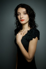 Naklejka premium Portrait of amazing young brunette woman with red sensual lips posing on black background in studio and touching her neck.