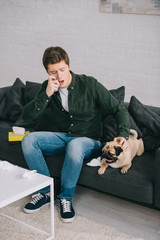 handsome man allergic to dog using inhaler while sitting on sofa and looking at pug