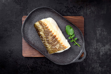 Fried Japanese skrei cod fish filet with wasabi lettuce as top view on a modern design plate