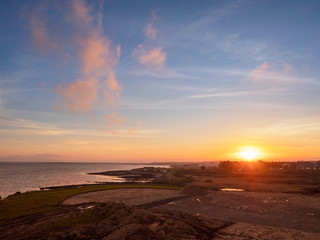 Obraz premium Sunset over Galway Bay, Galway city, Ireland, Warm and cool tones, sun flare, simple and calm scene. Atlantic ocean.