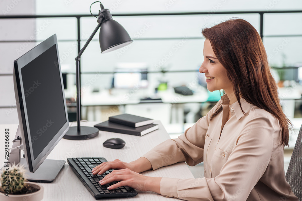 Wall mural smiling young woman typing on computer keyboard at workplace in modern office