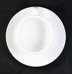Coffee and cream pouring into a white cup on a white saucer with a black background