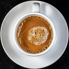 Coffee and cream pouring into a white cup on a white saucer with a black background