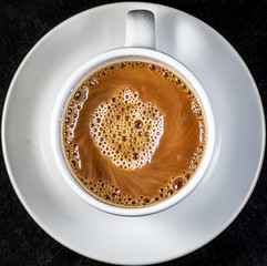 Coffee and cream pouring into a white cup on a white saucer with a black background