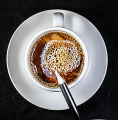 Coffee and cream pouring into a white cup on a white saucer with a black background