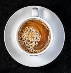 Coffee and cream pouring into a white cup on a white saucer with a black background
