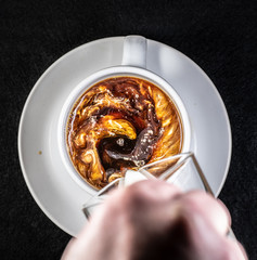 Coffee and cream pouring into a white cup on a white saucer with a black background