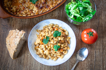Stewed and baked white beans with spices in a plate and lettuce and tomato salads with homemade bread on wooden table