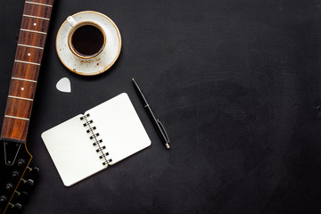 Naklejka premium Musician work place with guitar, notebook and coffee on black background top view mock up
