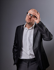 Fototapeta premium Thinking bald business man looking up serious in eyeglasses and have an idea in suit on grey background. Closeup