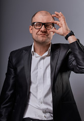 Thinking bald business man looking serious in eyeglasses in suit on grey background. Closeup