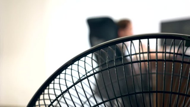 close-up of part of an office fan, on the background of a blurred writing desk, at which a person works at a computer