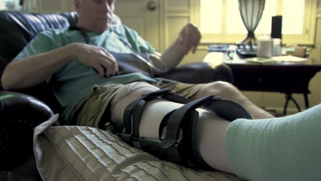man laying in an easy chair with leg brace in pain